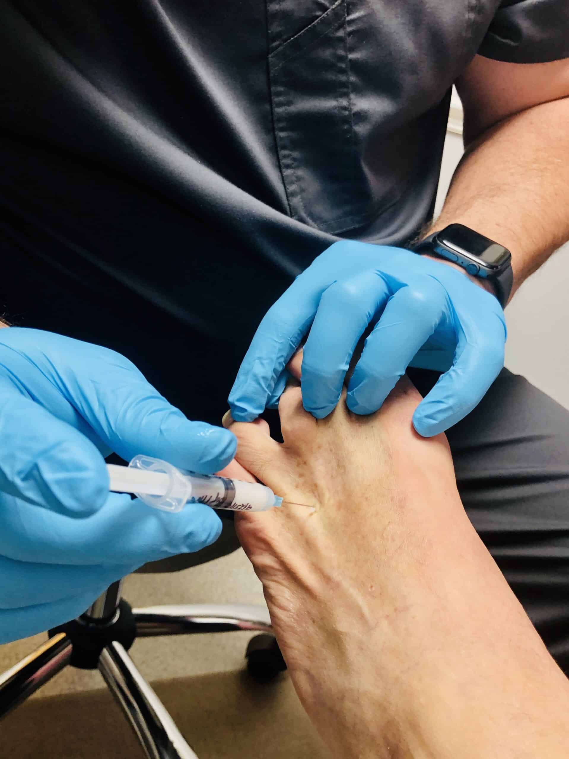 The patient getting a shot in his foot by the doctor